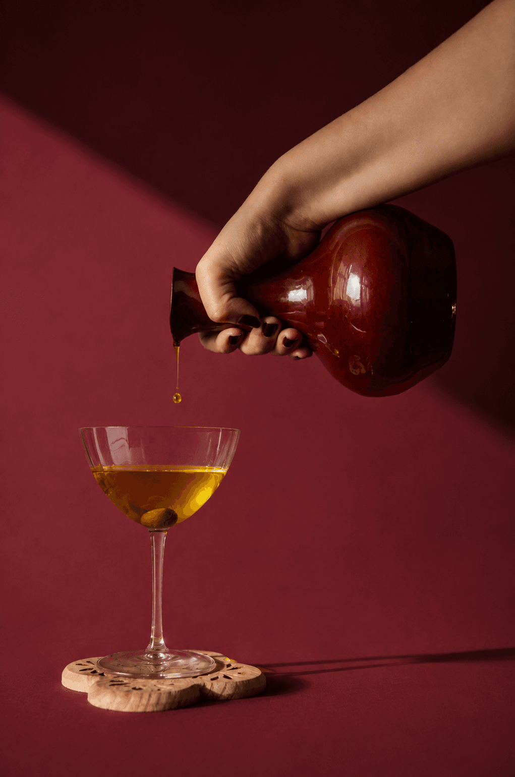 Oil poured from the Bri' Zeit carafe into a coupe glass on an oxblood ground
